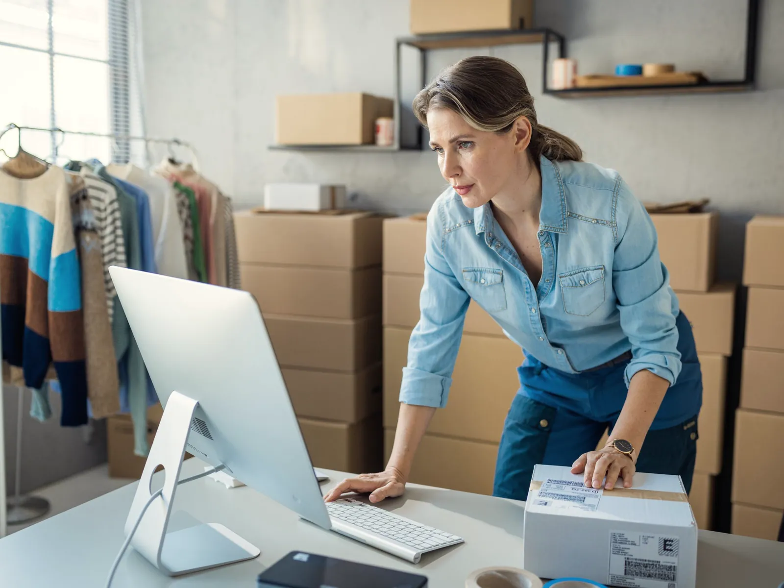 Online retailer processing orders at her computer in a stockroom