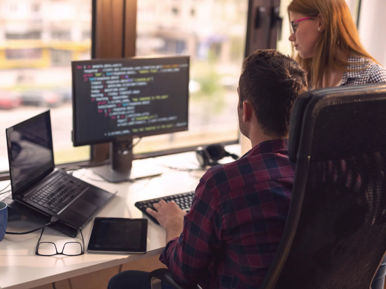 Two software developers working at a desk with code on screen